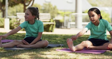 Diverse schoolgirls stretching on school lawn during outdoor kids yoga class