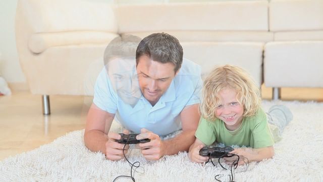 Father and son are enjoying a gaming session together on a comfortable carpet in their living room, highlighting family fun and togetherness. The image is perfect for use in advertisements or articles about family activities, gaming experiences, or bonding moments between parents and children. It captures a playful and joyful atmosphere, ideal for promoting family-friendly products or services.