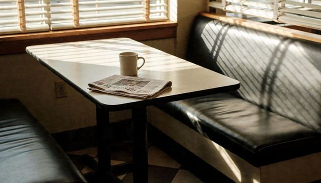 Sunlit diner booth with coffee cup and morning newspaper casting blinds shadow