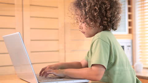 Curly-Haired Boy Focused On Typing At Home