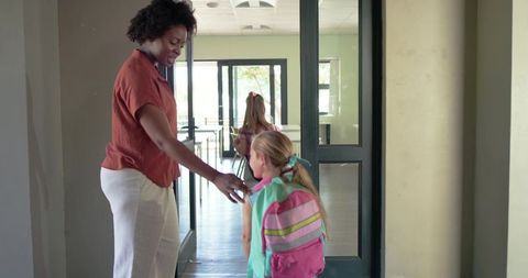 African american teacher greeting elementary student with pink backpack at school entrance