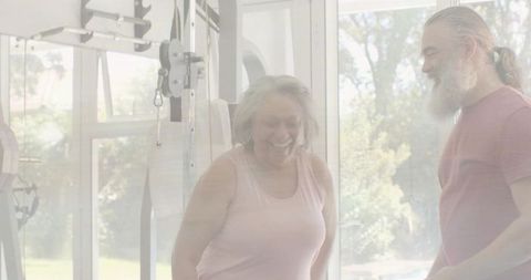 Senior woman strengthening body on cable machine with personal trainer in sunlit studio