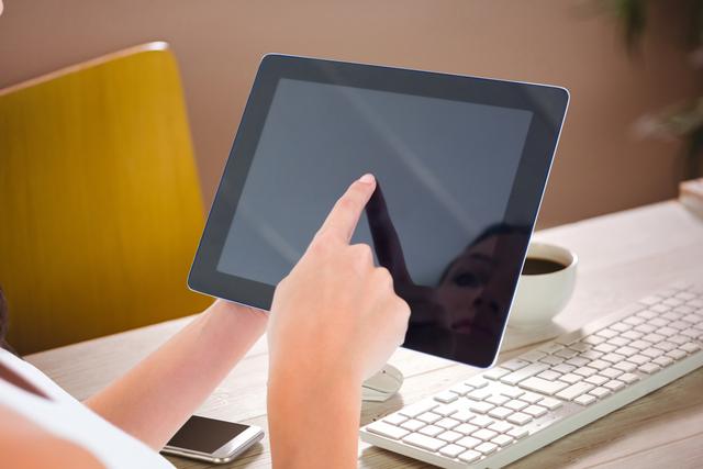 Close-up view of a woman interacting with a touchscreen tablet, which has a reflective screen. Ideal for use in technology, business, and remote work scenarios. Suitable for depicting themes related to modern technology, digital devices, and work environments.