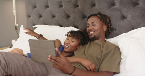 African american couple cuddling in bed watching tablet and smiling together