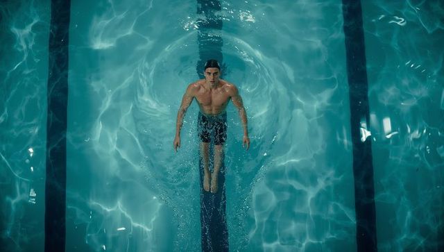 Top-down male swimmer powering through pool lane creating symmetric water ripples