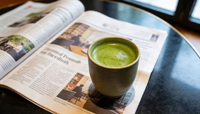 Frothy matcha latte in ceramic cup resting on newspaper by window for minimalist morning