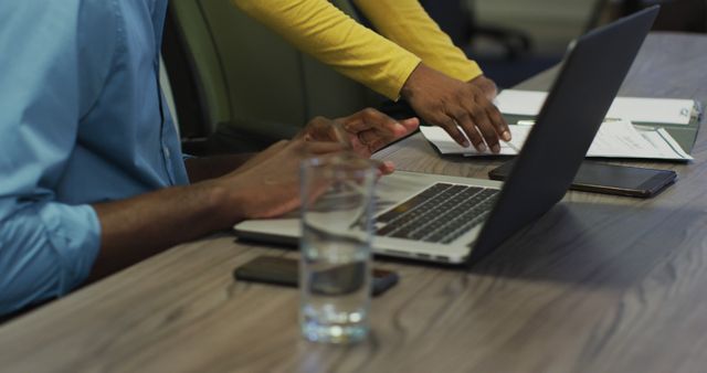 Business colleagues discussing a project with a laptop and documents on a desk, emphasizing teamwork and collaboration in a corporate environment. Ideal for use in business presentations, teamwork and collaboration-themed materials, office-related advertisements, or workplace productivity articles.