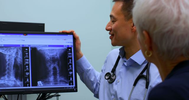 Young Asian male doctor discussing over x-ray report on computer at clinic. Senior patient looking at report 4k