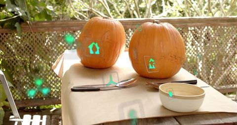 Outdoor pumpkin carving scene with augmented reality stencil icons on kraft-covered table