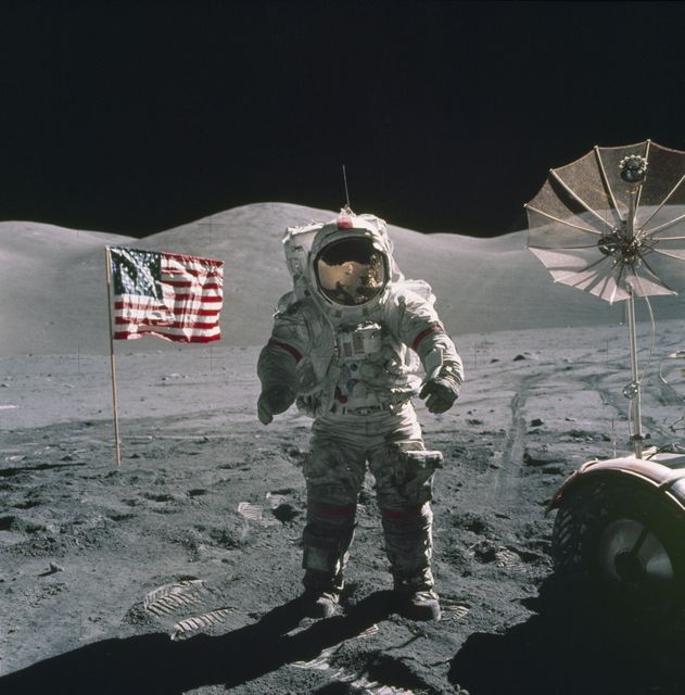 This is an Apollo 17 Astronaut standing upon the lunar surface with the United States flag in the background. The seventh and last manned lunar landing and return to Earth mission, the Apollo 17, carrying a crew of three astronauts: Mission Commander Eugene A. Cernan; Lunar Module pilot Harrison H. Schmitt; and Command Module pilot Ronald E. Evans lifted off on December 7, 1972 from the Kennedy Space Flight Center (KSC). Scientific objectives of the Apollo 17 mission included geological surveying and sampling of materials and surface features in a preselected area of the Taurus-Littrow region, deploying and activating surface experiments, and conducting in-flight experiments and photographic tasks during lunar orbit and transearth coast (TEC). These objectives included: Deployed experiments such as the Apollo lunar surface experiment package (ALSEP) with a Heat Flow experiment, Lunar seismic profiling (LSP), Lunar surface gravimeter (LSG), Lunar atmospheric composition experiment (LACE) and Lunar ejecta and meteorites (LEAM). The mission also included Lunar Sampling and Lunar orbital experiments. Biomedical experiments included the Biostack II Experiment and the BIOCORE experiment. The mission marked the longest Apollo mission, 504 hours, and the longest lunar surface stay time, 75 hours, which allowed the astronauts to conduct an extensive geological investigation. They collected 257 pounds (117 kilograms) of lunar samples with the use of the Marshall Space Flight Center designed Lunar Roving Vehicle (LRV). The mission ended on December 19, 1972