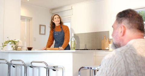 Couple talking in bright modern kitchen, woman holding rolling pin and smiling