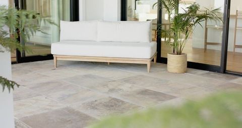Minimal outdoor lounge showing white two-seat sofa on stone tile patio with potted palm