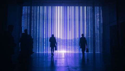 Silhouetted commuters walking through neon led portal with vertical blue light curtains
