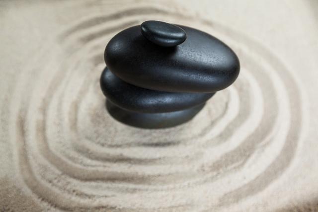 Stacked black pebble stones on rippled sand, symbolizing harmony and balance. Ideal for spa promotions, meditation concepts, or as a tranquil background. Visualizing calmness and relaxation.