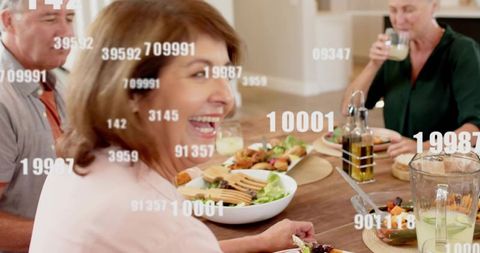 Laughing woman sharing family dinner with salad and floating numeric data overlays
