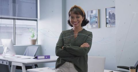 Smiling professional woman crossing arms in modern office with soft daylight and confident