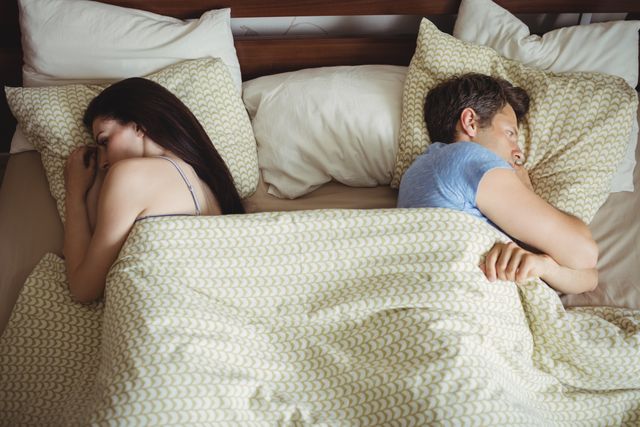 Couple sleeping back to back and ignoring each other on bed in bedroom