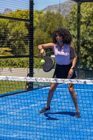 African american woman playing paddle tennis on vibrant blue court near net