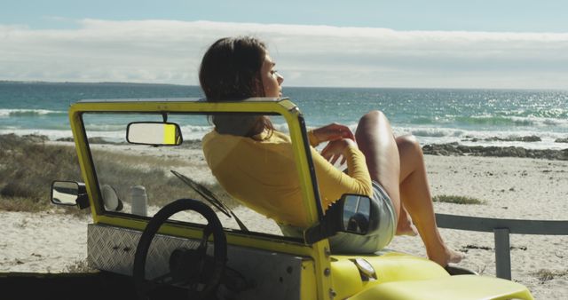 Woman relaxing in a yellow convertible car parked at the beach. Ideal for concepts related to summer vacations, carefree lifestyle, and outdoor leisure. Can be used for travel blogs, beach-themed advertisements, or lifestyle magazines.