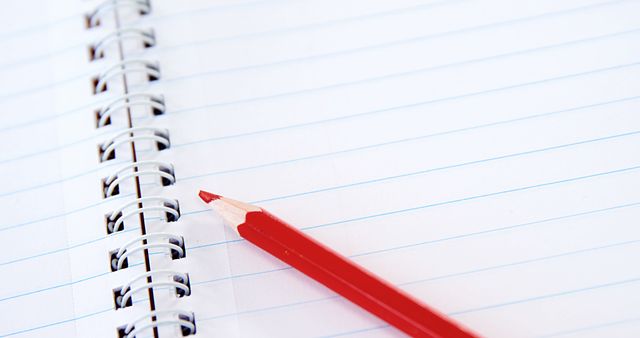 A red pencil lies on a lined spiral notebook, with copy space. Ideal for educational themes, this image evokes the concept of writing, note-taking, or studying.