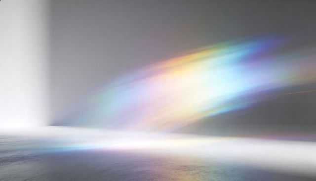 Soft prismatic light beam spreading across minimalist gallery floor with pastel spectrum