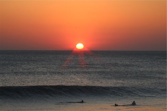 Serene Sunset Over Majestic Ocean with Surfers in Water - Download Free Stock Photos Pikwizard.com