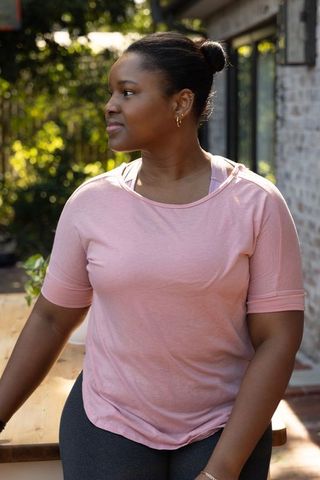 African american woman standing on sunlit deck wearing pink athleisure top and leggings