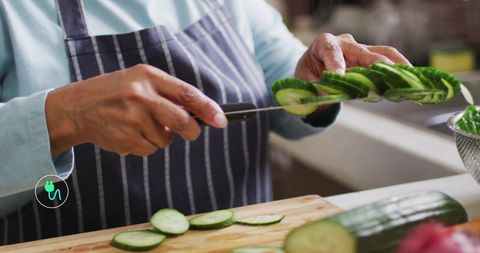 Senior indian cook slicing and stacking cucumber slices on wooden cutting board