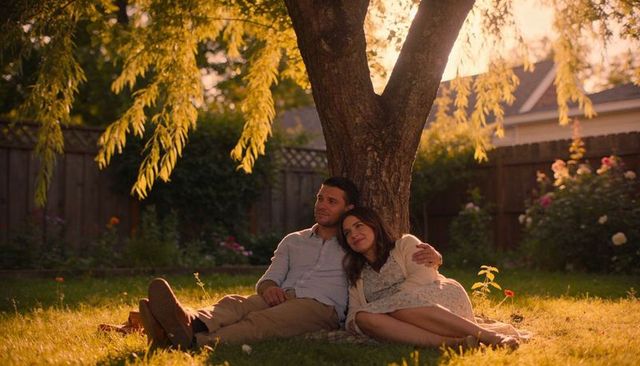 Couple leaning under tree sharing golden hour embrace in suburban backyard garden at sunset