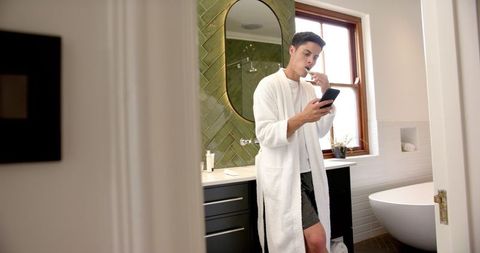 Man Multitasking with Toothbrush and Smartphone in Modern Bathroom