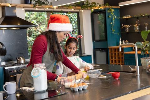 Asian mother and daughter baking christmas cookies together in cozy teal kitchen island