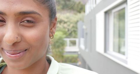 Indian woman smiling on balcony with nose stud and hoop earring, soft natural light