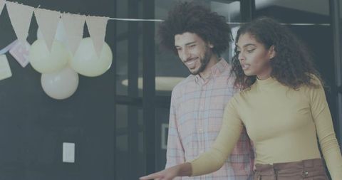 Young professionals collaborating and pointing during office celebration with balloons