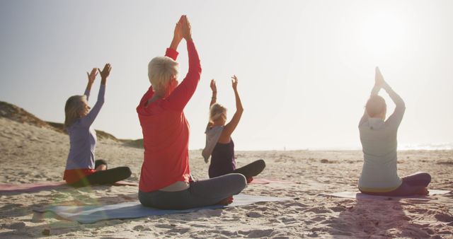Senior women sit on beach mats meditating in yoga poses under morning sun. Use this to promote yoga classes, healthy lifestyles, or senior fitness programs. Ideal for advertisements or well-being blogs focusing on outdoor group activities for older adults.