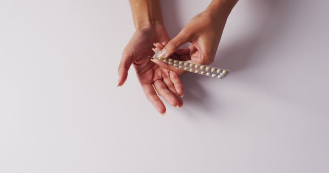 This image shows an individual holding a pill blister pack while dispensing a pill into their hand. Ideal for use in medication instructions, health articles, pharmaceutical advertisements, and self-care topics.