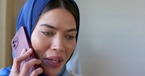 Indian woman in blue hijab talking on mauve smartphone with nose stud and ring close-up