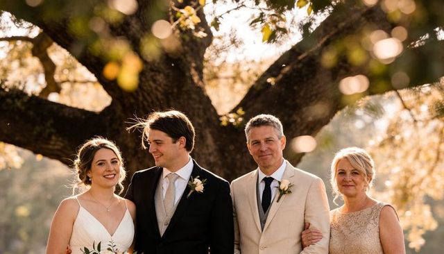 Golden-hour wedding portrait with bride and groom posing with parents under oak tree