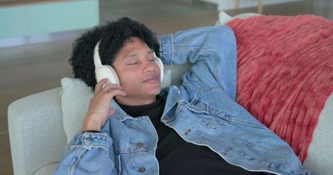 Relaxed african american man listening to music with headphones on modern sofa