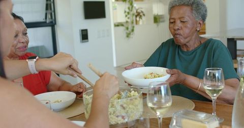 Senior african american women serving pasta salad and sharing warm family dinner moments