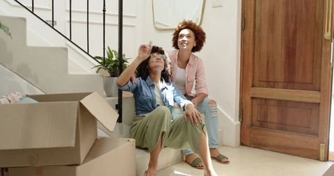 African american friends unpacking in new home sitting on stairs enjoying sunlight