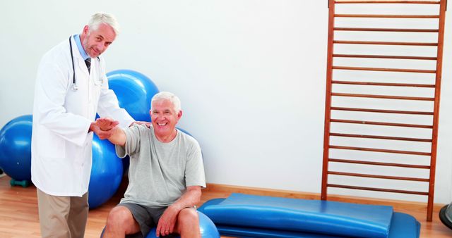 Elderly man receiving physical therapy from therapist in clinic. Patient sitting on exercise ball, therapist holding patient's arm. Ideal for use in healthcare advertisements, senior care promotions, and physical therapy informational materials.