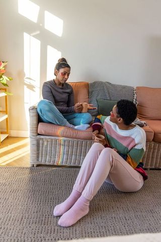 Sunlit cozy conversation: indian and african american women sipping coffee on wicker couch