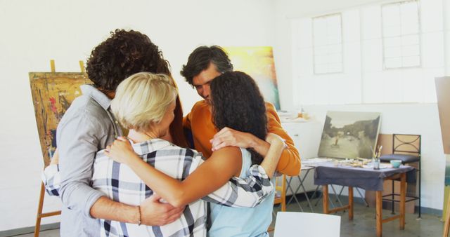 Diverse group of adults embracing in art studio surrounded by paintings and art supplies. Perfect for illustrating themes of teamwork, support, creativity, and collaborative projects in artistic or educational environments.