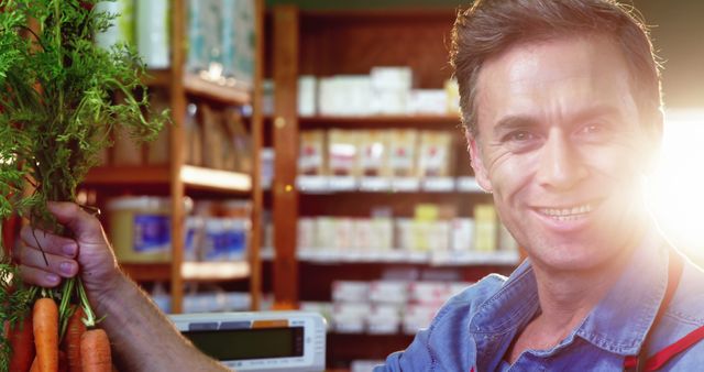 Smiling Shopkeeper Holding Fresh Carrots in Grocery Store - Download Free Stock Images Pikwizard.com