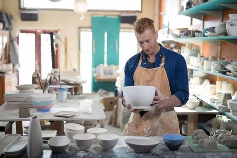 Artisan Potter Inspecting Ceramics in Sunlit Studio