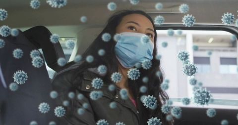 Woman wearing surgical mask sitting in backseat with floating virus particle overlay