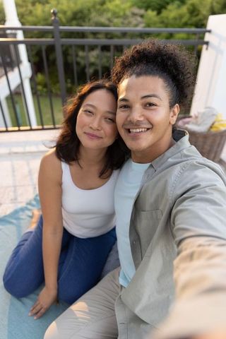 Young couple taking selfie on balcony picnic relaxing together at sunset