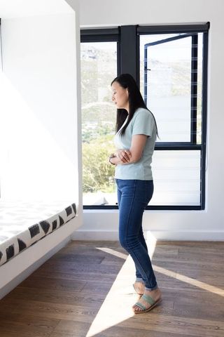 Mature african woman standing by sunlit window in minimalist bedroom, contemplative solitude