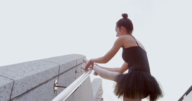 Ballerina stretches at an outdoor railing, with copy space. Her poise and focus suggest a dedication to the art of ballet.