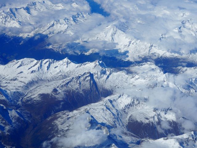 Breathtaking aerial view showcasing snow-capped mountain peaks blanketed by clouds. Ideal for travel magazines, geography books, climate studies, outdoor adventure promotions, and winter season backdrops or screensavers.